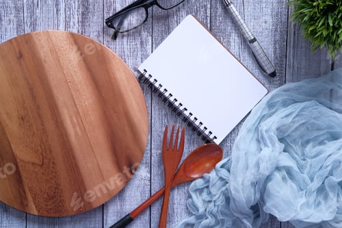 Preview: Notepad and chopping board with wooden fork and spoon on white table.
