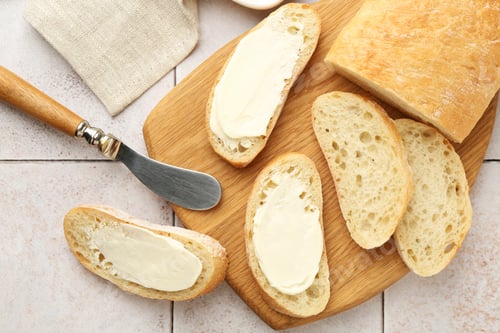 Preview: Pieces of bread with butter and knife on light tiled table, top view