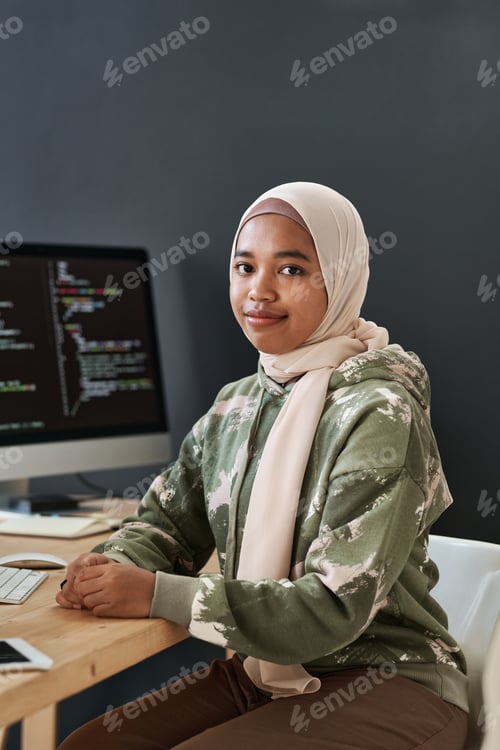 Preview: Young successful Muslim businesswoman in casualwear sitting by workplace