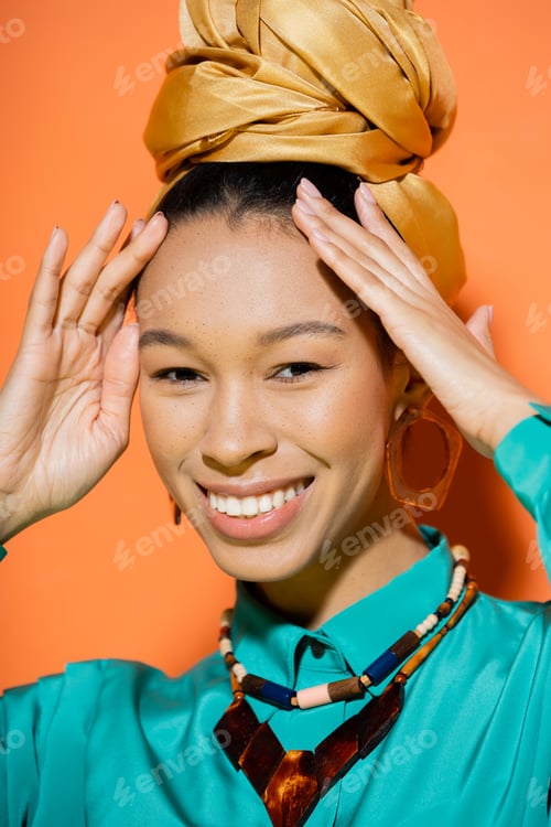 Preview: Portrait of fashionable african american woman in summer clothes touching hair on orange background