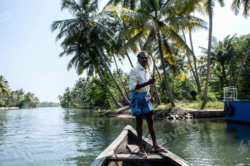 Preview: Man navigating a river on a wooden boat amidst lush greenery