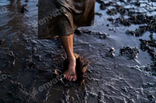 Preview: Bare feet of a dirty woman wading through mud puddles