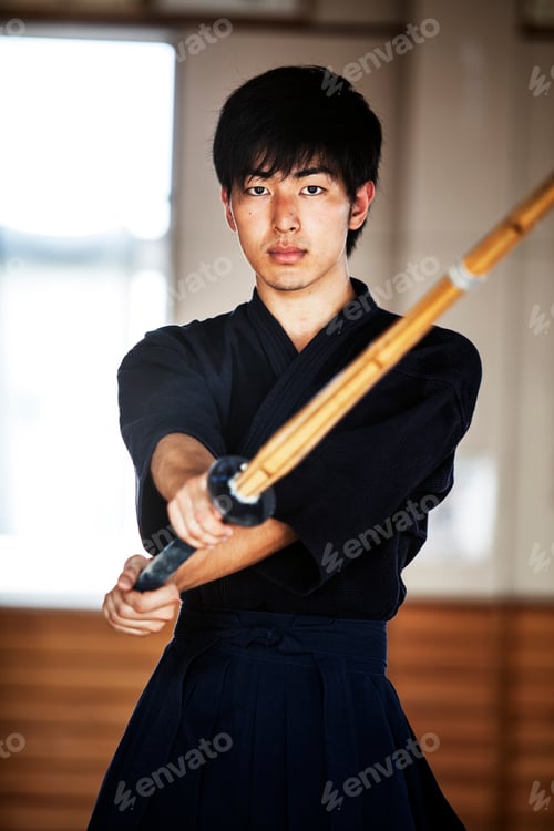 Preview: Male Japanese Kendo fighter holding wood sword in combat pose, looking at camera.