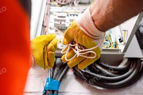 Preview: Cropped view of electrician in gloves holding wires near electrical box