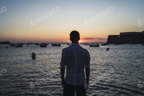 Preview: Horizontal shot of a man with white shirt looking to the seascape in the evening