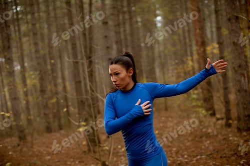 Preview: Young woman in blue track suit stretching before workout in the autumn forest