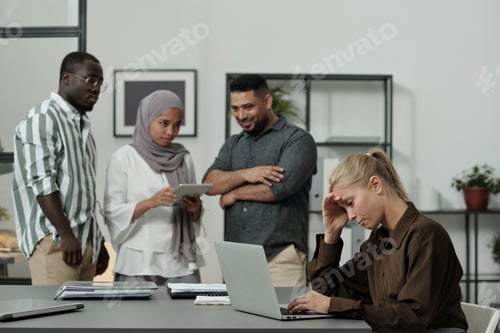 Preview: Young blond businesswoman touching head while sitting in front of laptop