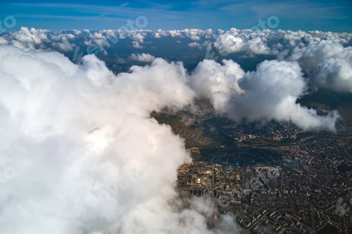 Preview: Aerial view from airplane window at high altitude of distant city covered with puffy cumulus clouds