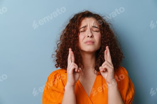 Preview: Unhappy redhead curly girl holding fingers crossed for good luck