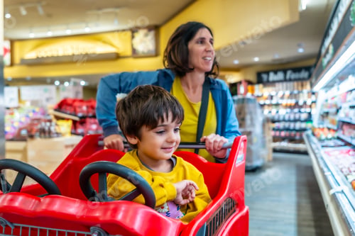 Preview: Mother pushing shopping cart with son sitting inside in supermarket