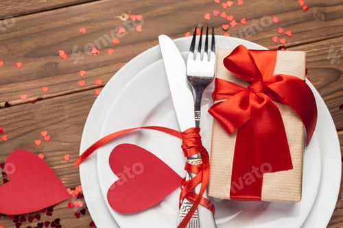 Preview: Romantic dinner setting with a gift wrapped in red ribbon and heart decorations