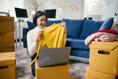 Preview: Asian woman selling clothes online using laptop at home office