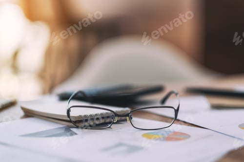 Preview: Close up image of black eyeglasses with paperwork on the table