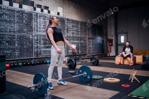Preview: Young man watching woman preparing to lift barbell in gym