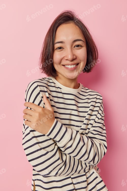 Preview: Pleased good looking Asian girl with dark hair smiles happily keeps arms half crossed looks