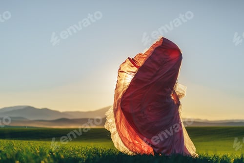 Preview: Girl in pink dress walking through green fields at sunset