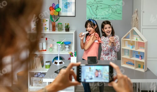 Preview: Teacher recording video in mobile phone of happy students singing using light bulbs as microphones