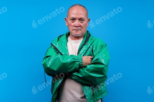 Preview: Confident Mature Asian Male With Serious Expression And Arms Crossed Over Blue Background