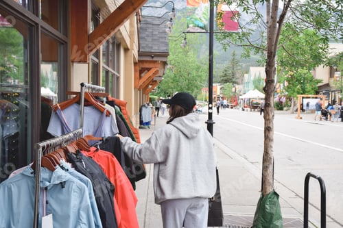 Preview: Young girl shopping for clothes on clothes rack outside a store on a street
