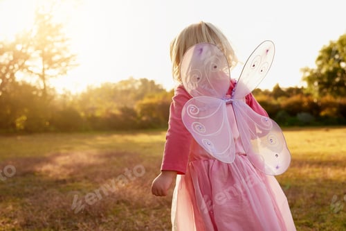 Preview: Rear view shot of a little girl dressed up as a fairy enjoying the day outside