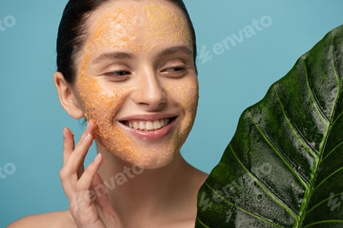Preview: smiling girl with sugar scrub on face holding leaf, isolated on blue