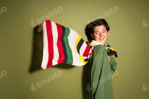 Preview: cheerful woman looking at striped multicolored scarf waving on wind on green background