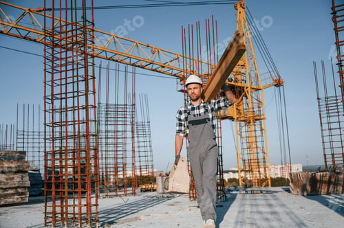 Preview: Crane behind. Holding wooden piece. Man is working on the construction site at daytime