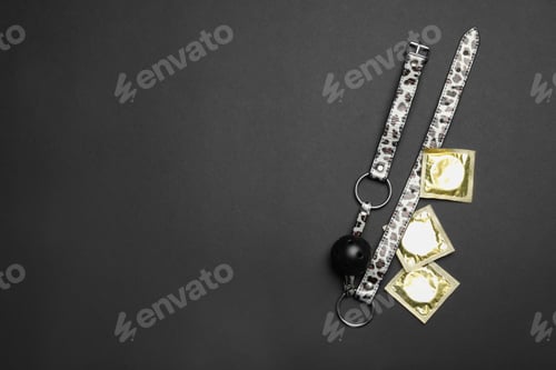 Preview: Ball gag and condoms on black background, top view with space for text. Sex game