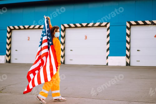 Preview: African American woman with medical face mask posing with american flag. Covid-2019.