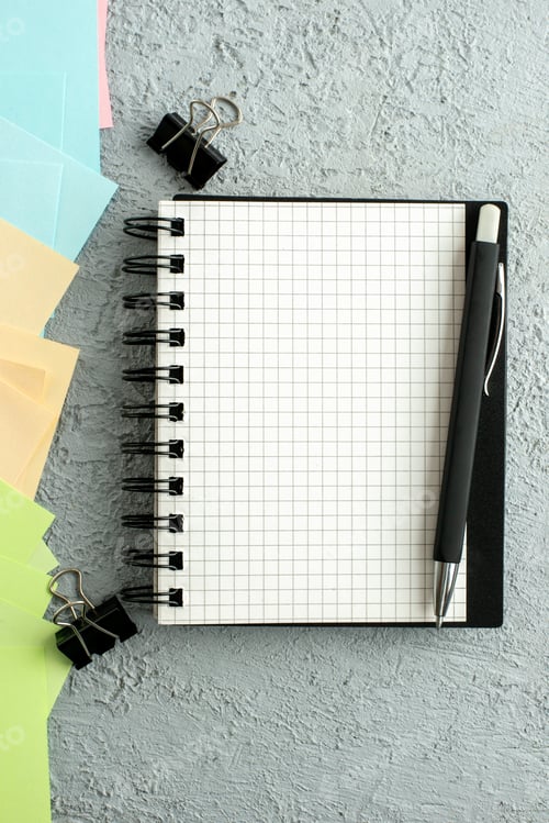 Preview: Vertical view of pen on spiral notebook on black book and coloured envelopes on gray distressed