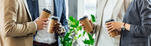 Preview: panoramic shot of four multiethnic colleagues holding disposable cups of coffee in office