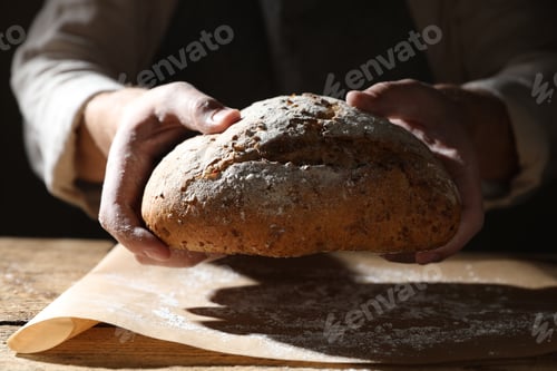 Preview: Man breaking loaf of fresh bread at wooden table, closeup