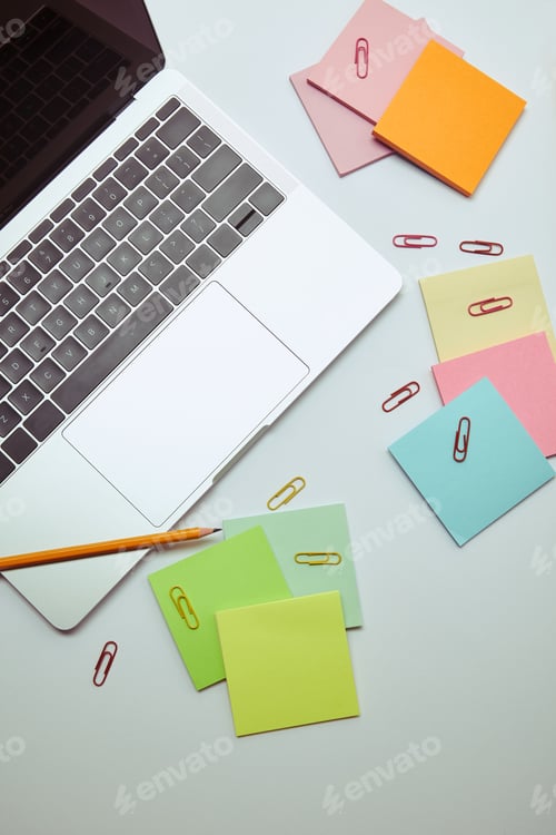 Preview: elevated view of laptop, paper stickers, pencil and paper clips on white tabletop
