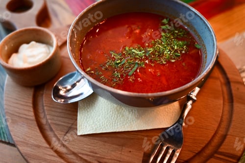 Preview: Russian traditional dish borscht with herbs and sour cream in a semicircular plate on a wooden board