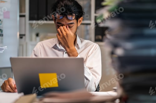 Preview: Exhausted Asain business man using laptop computer working in office.