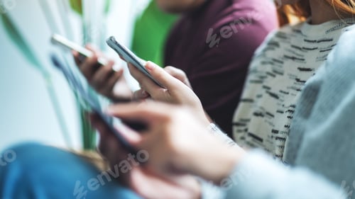 Preview: Group of young people using and looking at mobile phone while sitting together