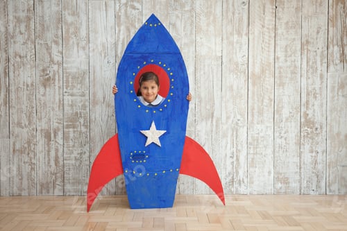 Preview: Portrait of girl looking from window of blue homemade cardboard rocket