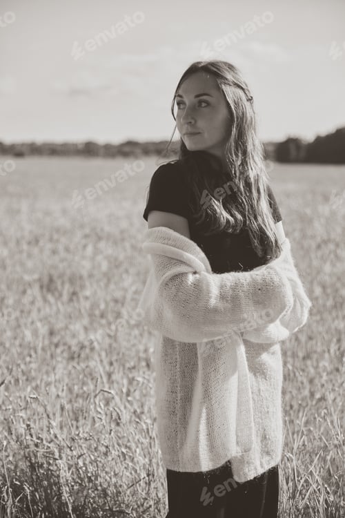 Preview: Young woman standing contemplatively in rye field under soft natural light