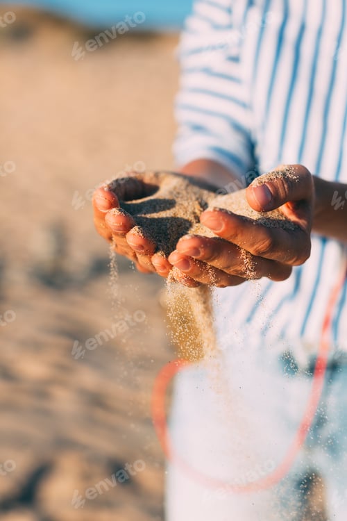 Preview: Woman on the beach letting sand trickling through her hands, close-up