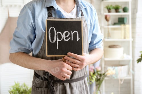 Preview: Male florist holding OPEN sign at workplace
