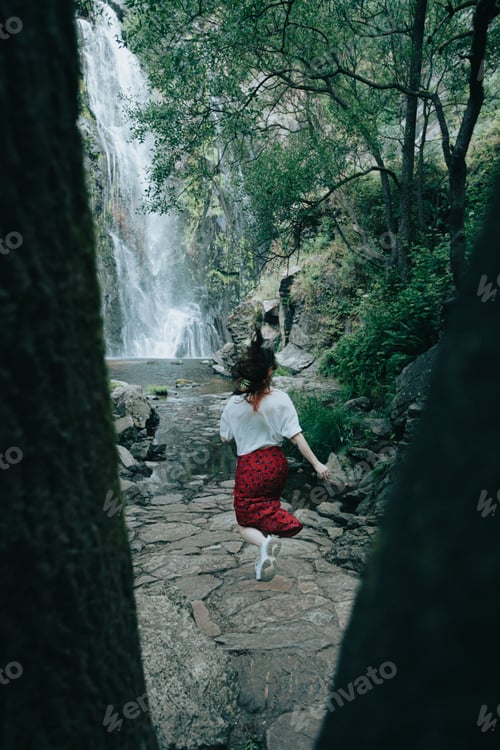 Preview: Young woman running towards a waterfall, close up between trees image