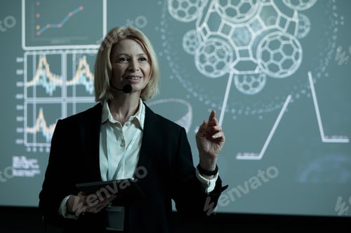 Preview: Confident mature female speaker with tablet and microphone by mouth