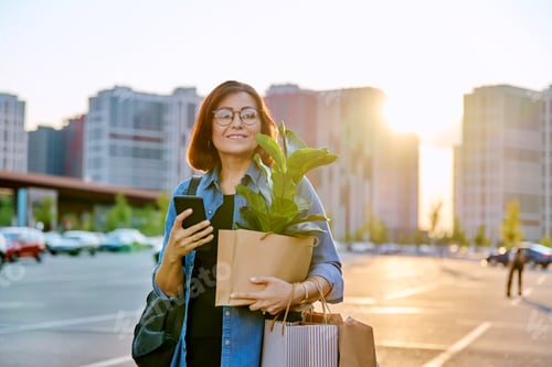 Preview: Woman with shopping paper bags, purchased plant walking outdoor