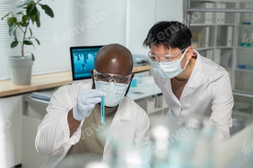 Preview: Two young interracial chemists looking at blue liquid in test tube