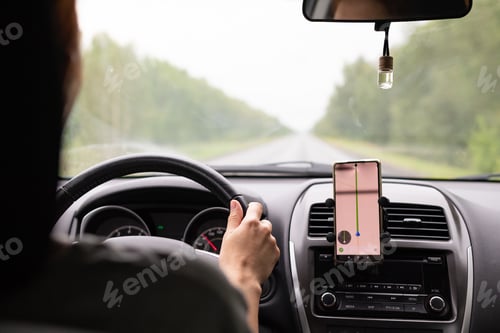 Preview: Rear view of a young traveler using a navigator on a mobile phone behind the wheel of a modern car .