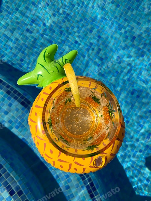 Preview: Glass of sparkling water and slice of lemon in an inflatable pineapple drink holder floating in a