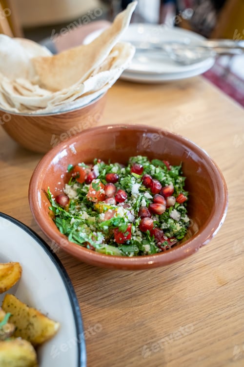 Preview: Close-up of a tasty tabbouleh salad with pomegranate seeds in a brown ceramic bowl
