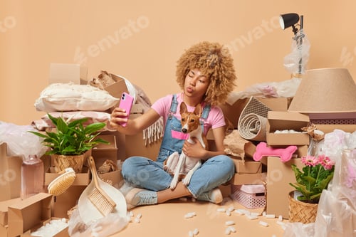 Preview: Moing housing ownership and real estate concept. Curly haired young woman poses with pet dog winks e