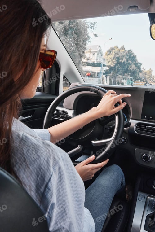 Preview: Woman driving car, focused on dashboard screen, hands on steering wheel, showcasing modern