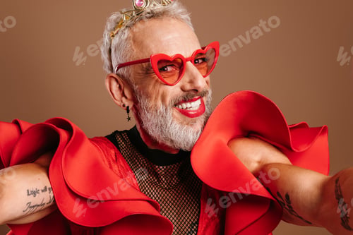 Preview: Happy mature gay man in beautiful red dress making self portrait against brown background